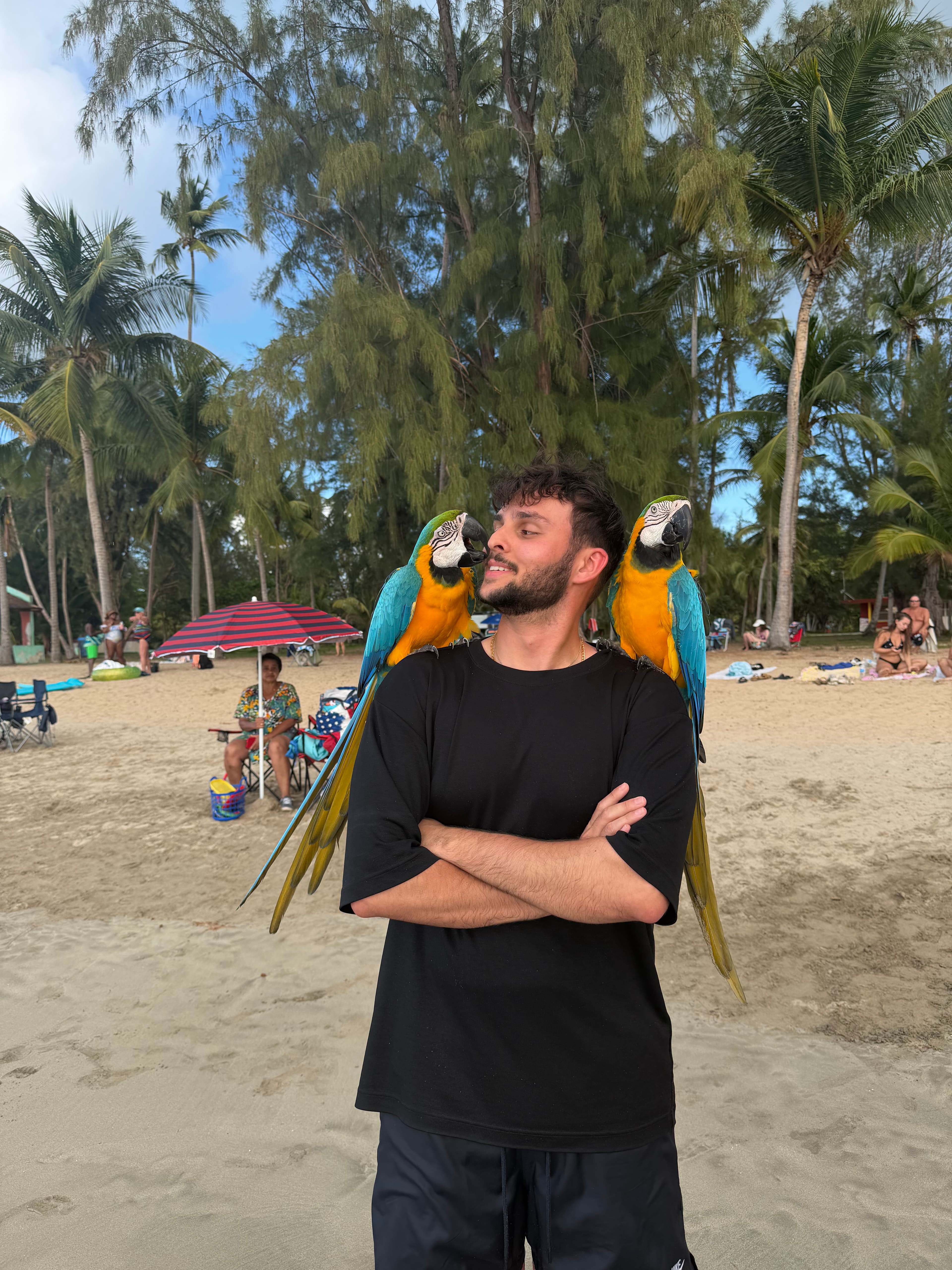 John V. Pereira with two parrots on his shoulders at the beach